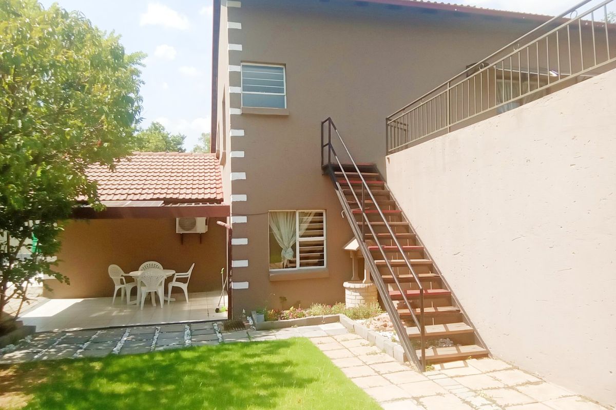 Rear exterior view featuring a covered patio, a lawn area, and an external staircase leading to an upper level.