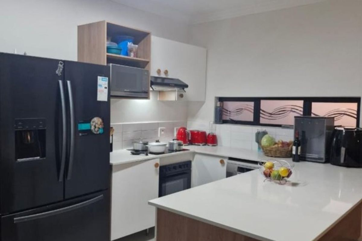 A modern kitchen featuring white cabinetry, a central island with a stone countertop, built-in oven, extractor fan, and tiled flooring.