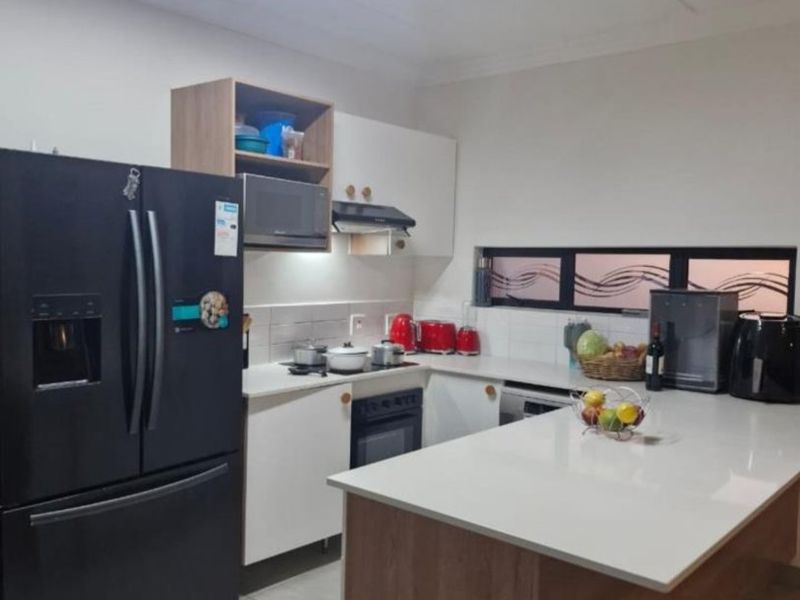 A modern kitchen featuring white cabinetry, a central island with a stone countertop, built-in oven, extractor fan, and tiled flooring.