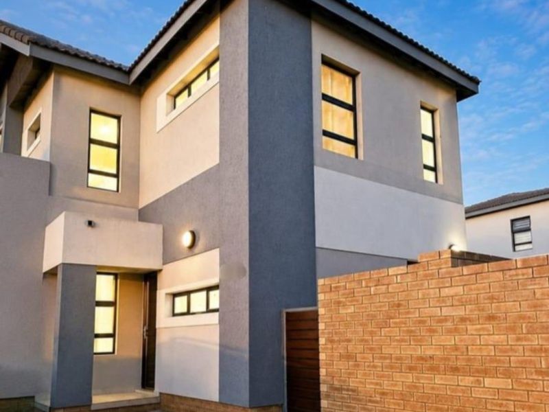 Modern two-story residential facade featuring a contemporary grey and white exterior finish, tiled roof, and a brick boundary wall.