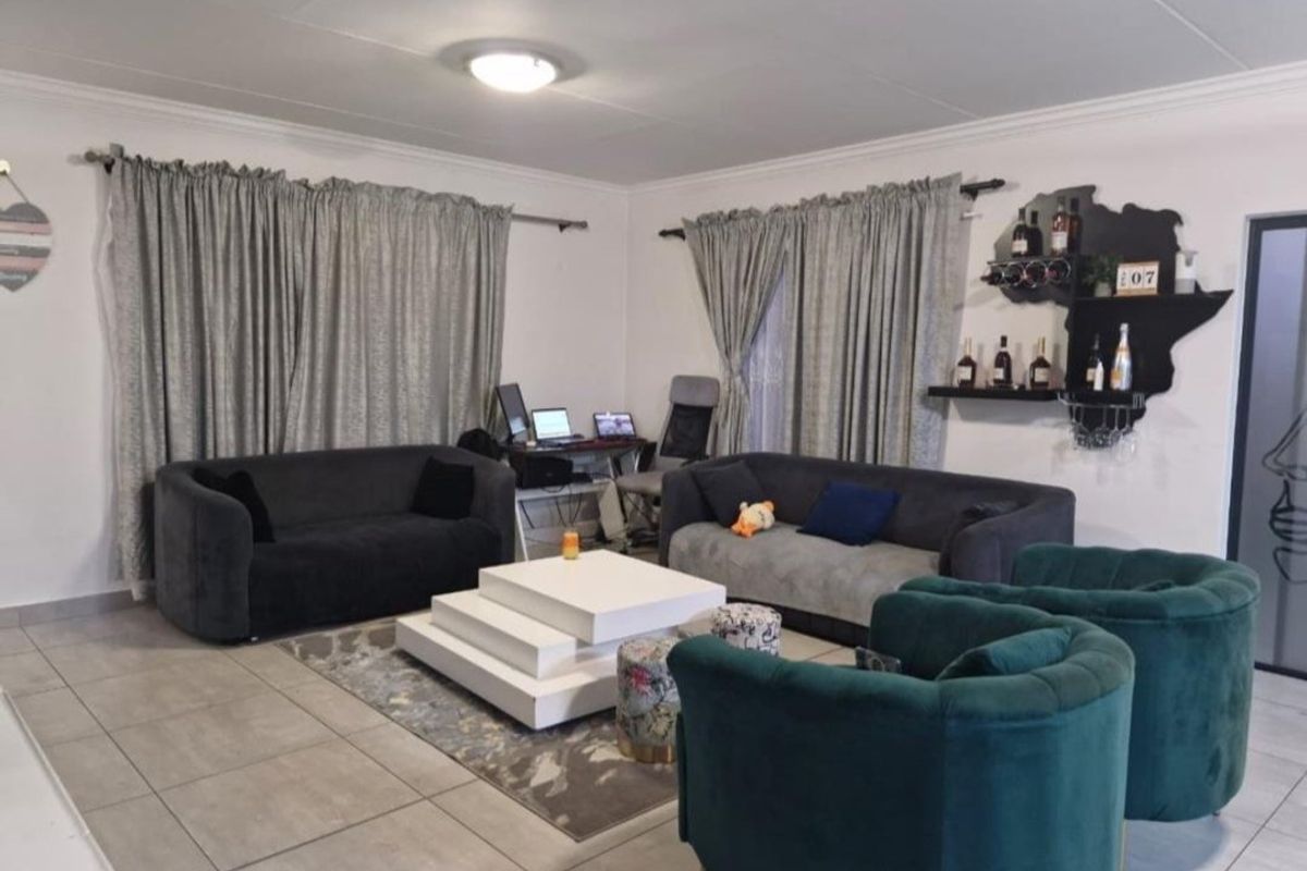 A spacious living room featuring neutral floor tiles, coved ceilings, and large windows dressed with curtains.