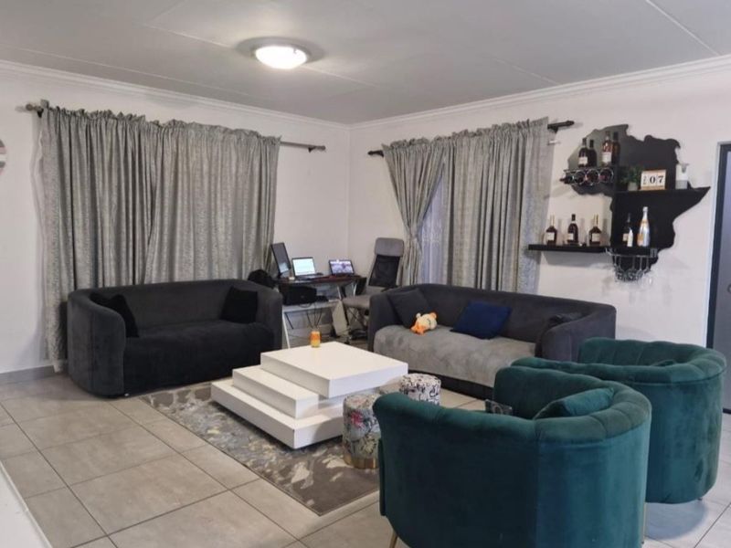 A spacious living room featuring neutral floor tiles, coved ceilings, and large windows dressed with curtains.