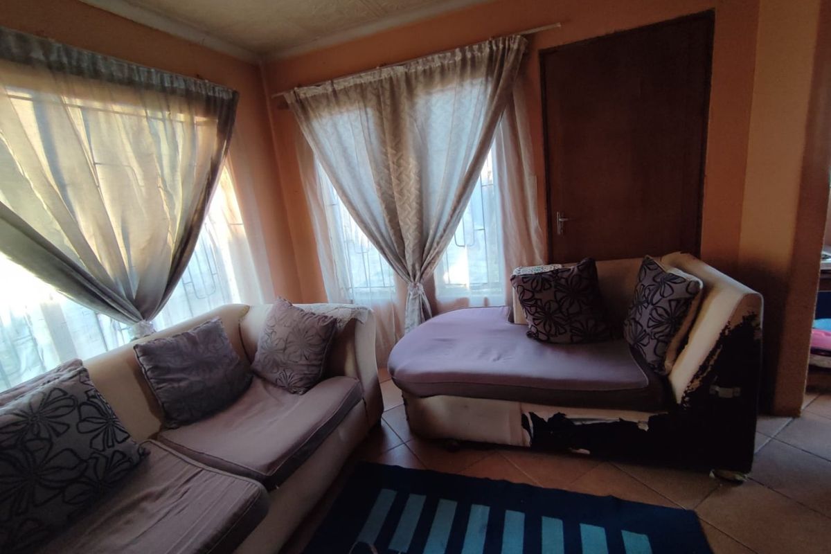 A living room area featuring tiled flooring and large windows with curtains, providing natural light to the space.