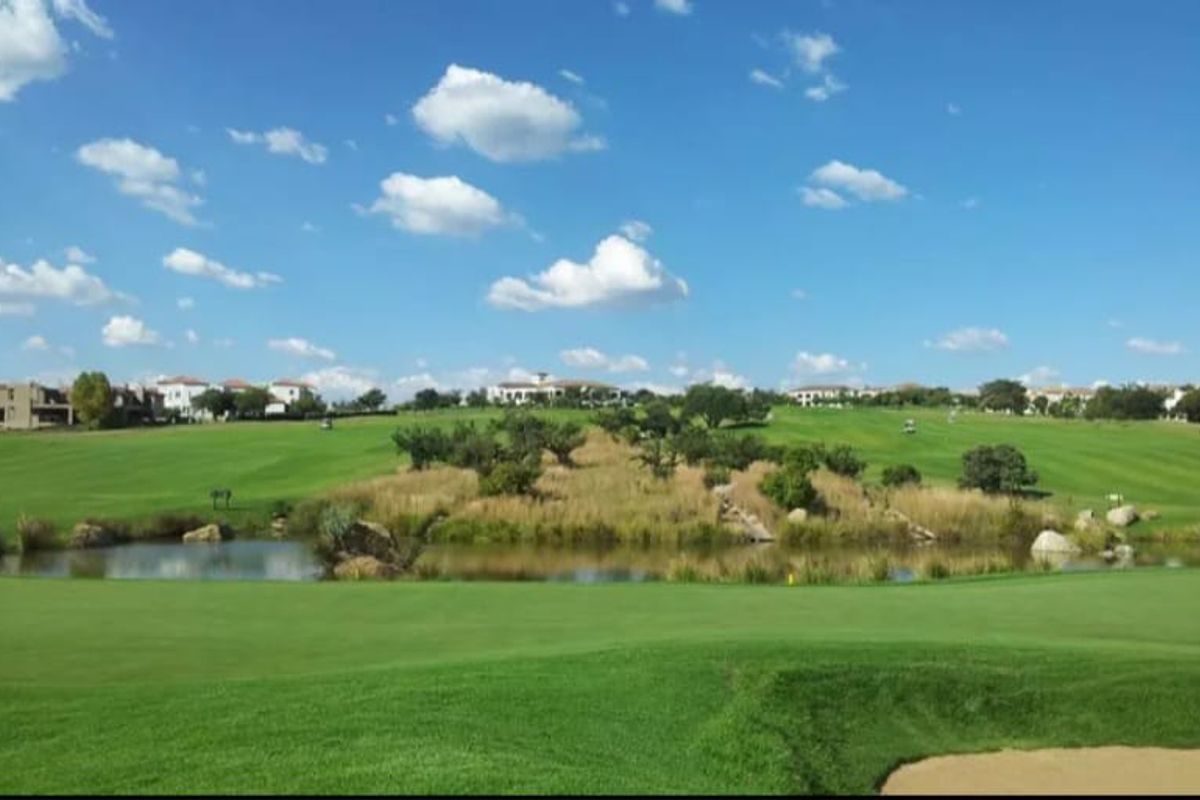 A scenic view of a well-maintained golf course landscape featuring a small pond, manicured greens, and surrounding residential estate properties.