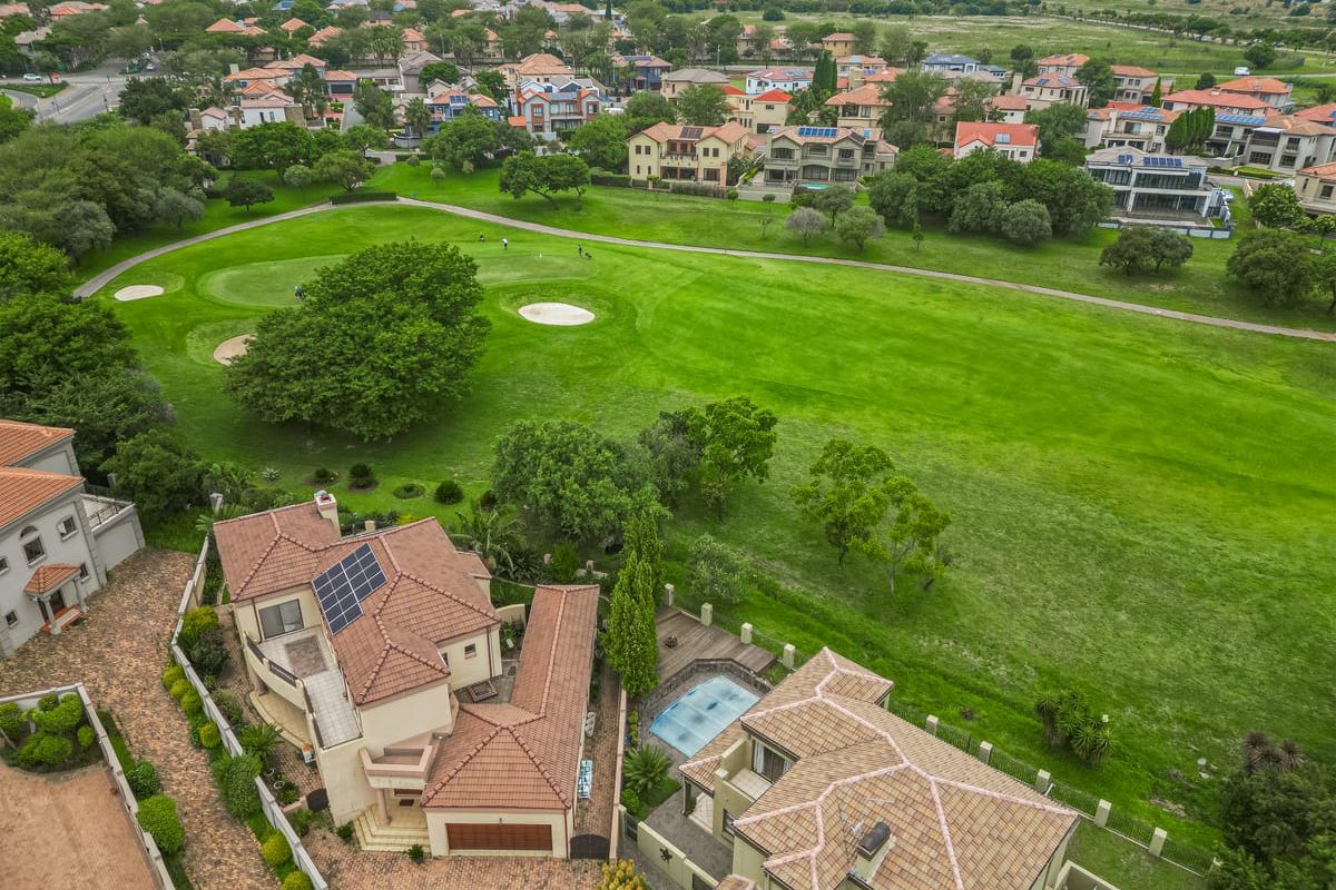 Aerial view of a residential property featuring a tiled roof, solar panels, and a swimming pool, overlooking a lush green golf course.