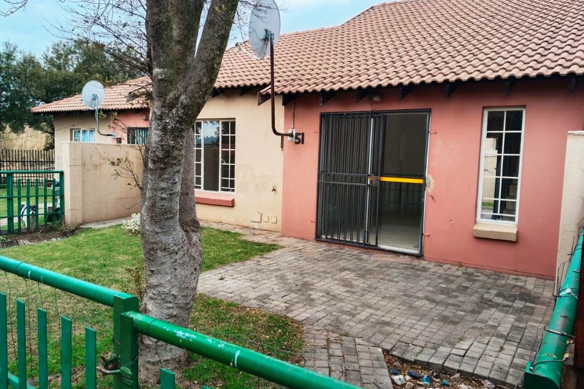 Rear view of a townhouse featuring a paved patio area, small garden, and security gate access to the living space.