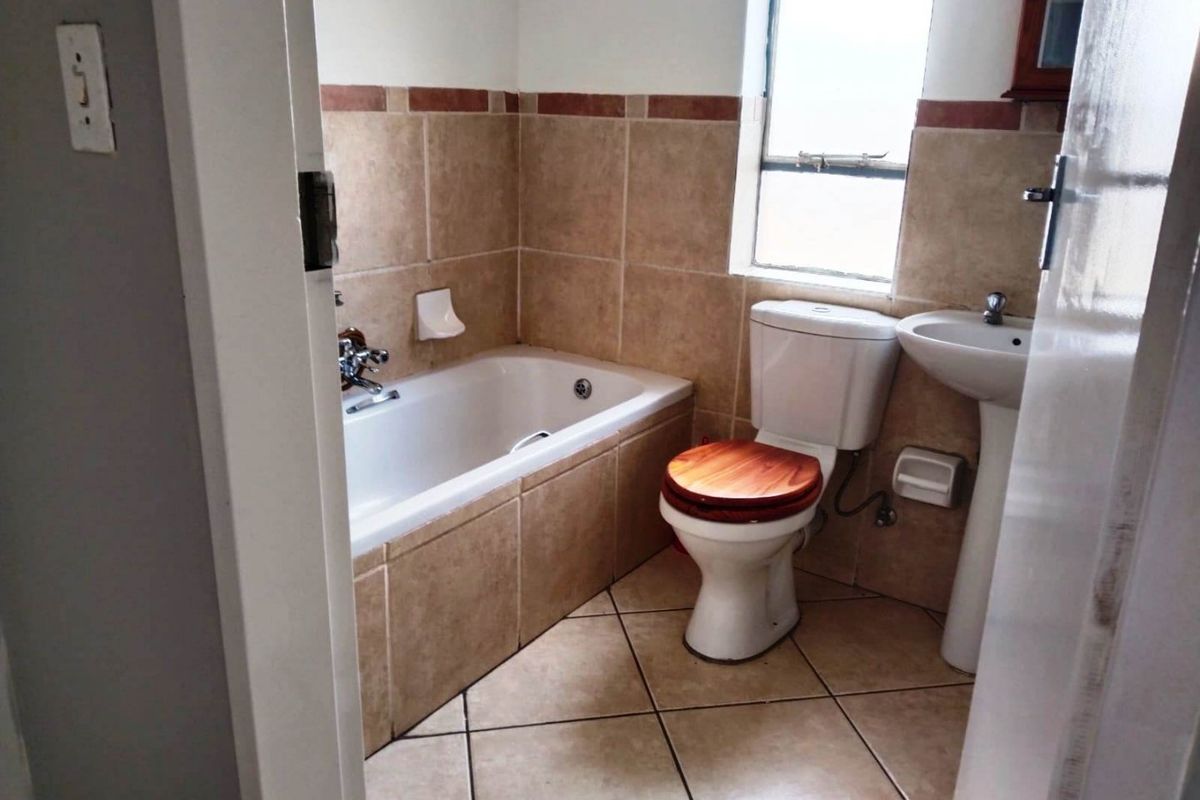 A functional bathroom featuring a built-in bathtub, pedestal basin, and toilet with neutral wall and floor tiling.