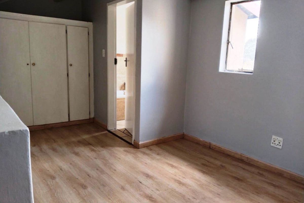 A bright, empty bedroom featuring light wood-look flooring, built-in cupboards, and direct access to an adjoining bathroom.