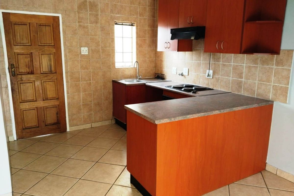 A functional kitchen featuring wood-look cabinetry, a built-in hob, extractor fan, and tiled flooring with a neutral splashback.