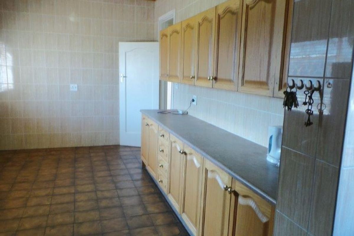 A dated kitchen featuring wooden cabinetry, tiled walls, and tiled flooring, offering a functional layout ready for modernization.