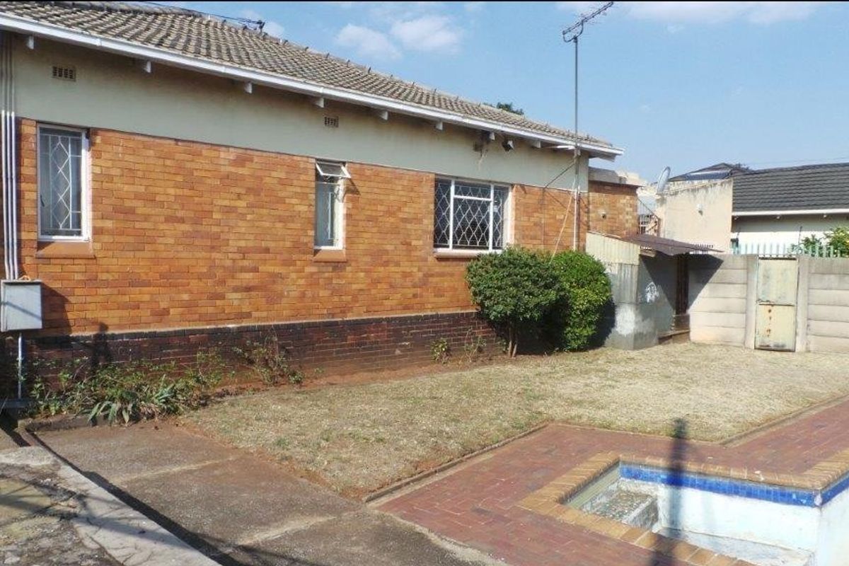 Rear exterior view of a brick house featuring a swimming pool, paved patio area, and a small garden space.