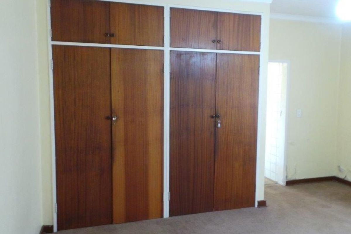 Bedroom featuring built-in wooden cupboards with overhead storage compartments and carpeted flooring.