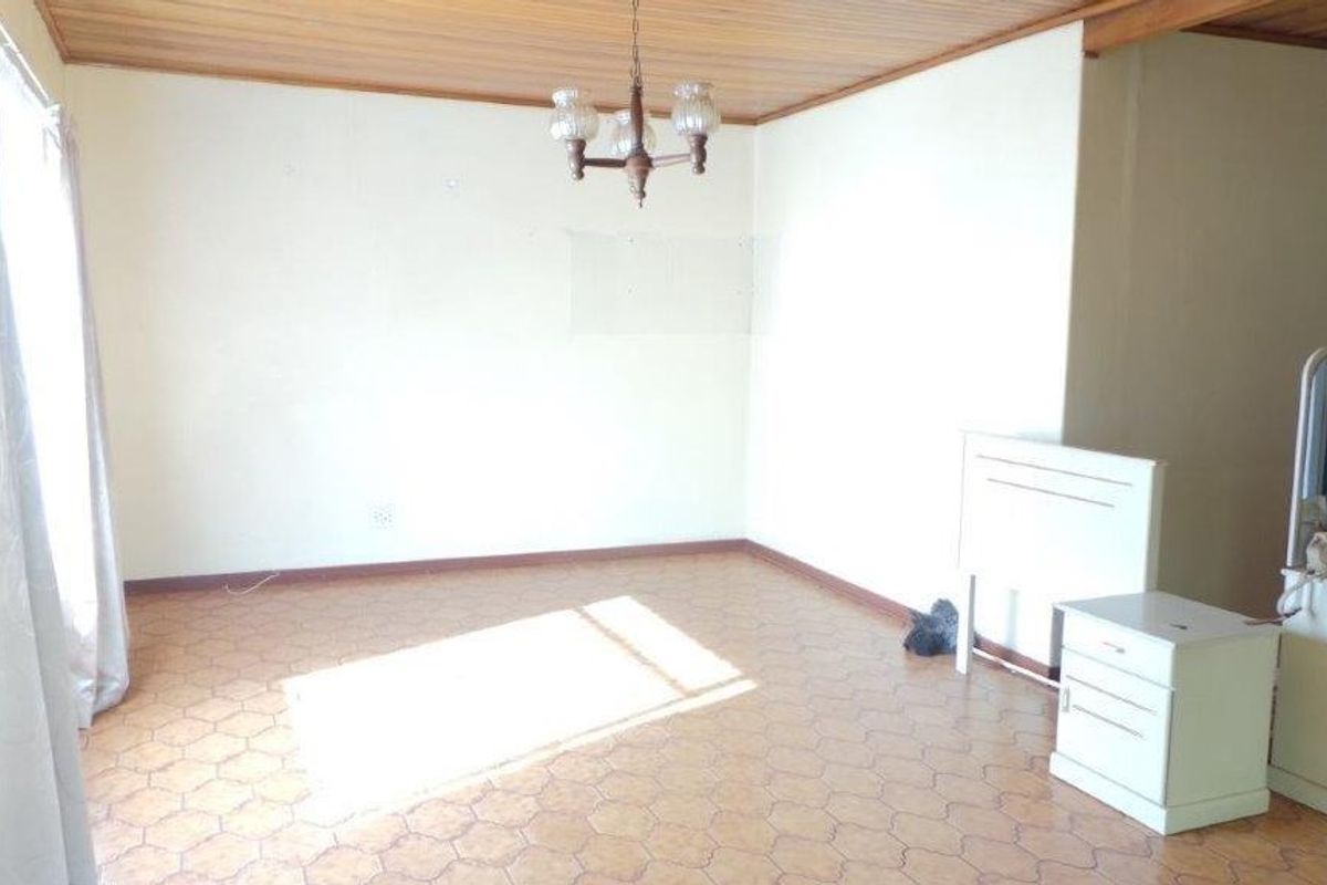 A spacious living area featuring a timber-paneled ceiling, vinyl flooring, and a central light fixture, offering a blank canvas for renovation.