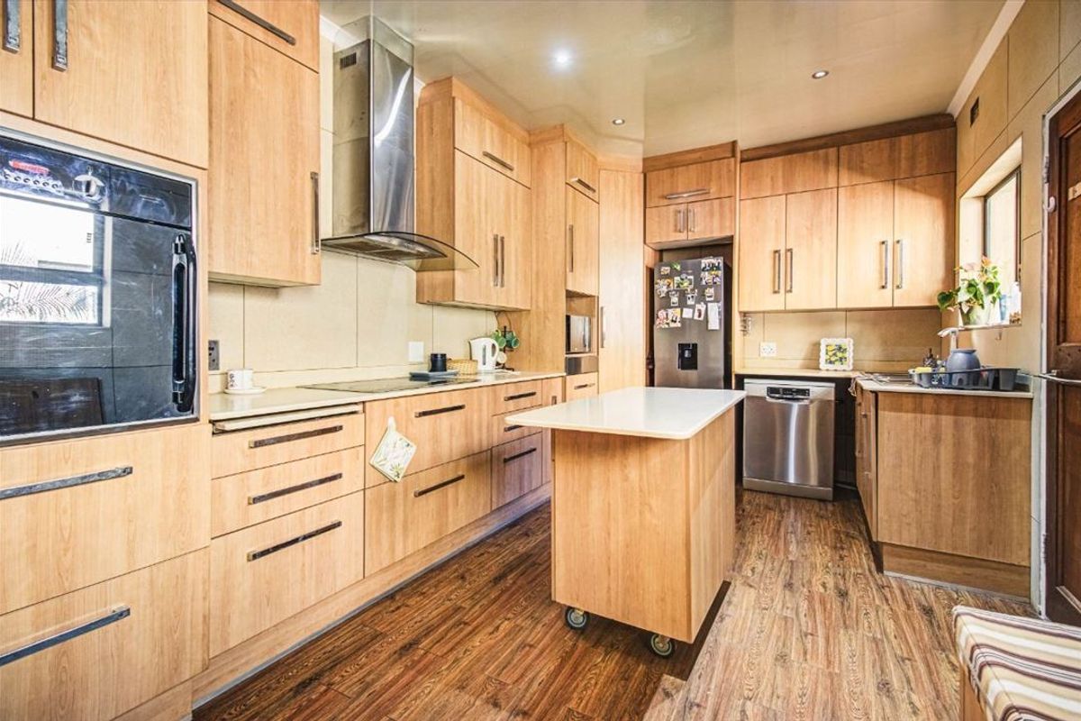 A functional kitchen featuring light wood cabinetry, a stainless steel extractor fan, built-in oven, and a central mobile island unit.