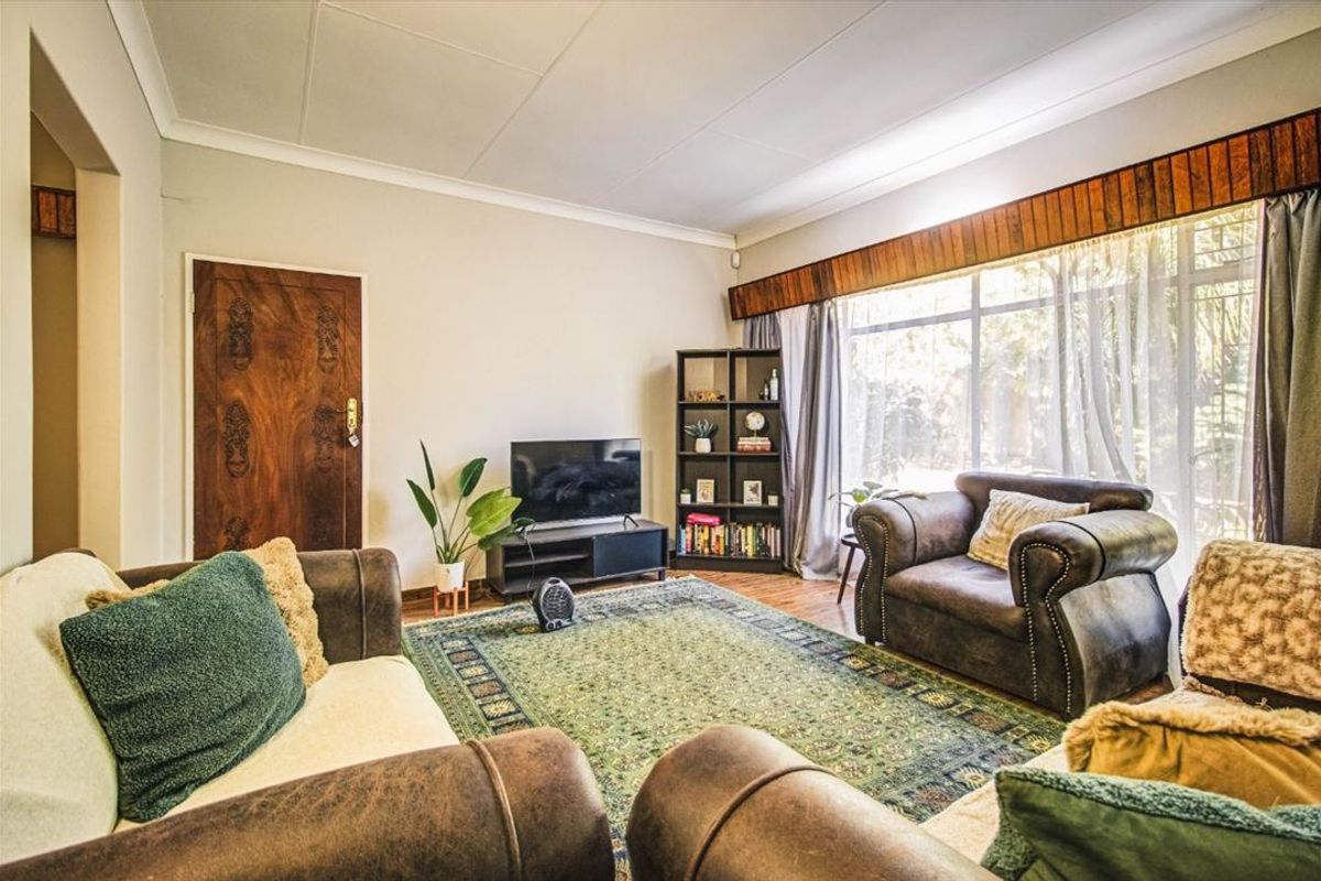 A living room featuring large windows with wooden pelmets, coved ceilings, and wood-look flooring, providing a comfortable and functional space.