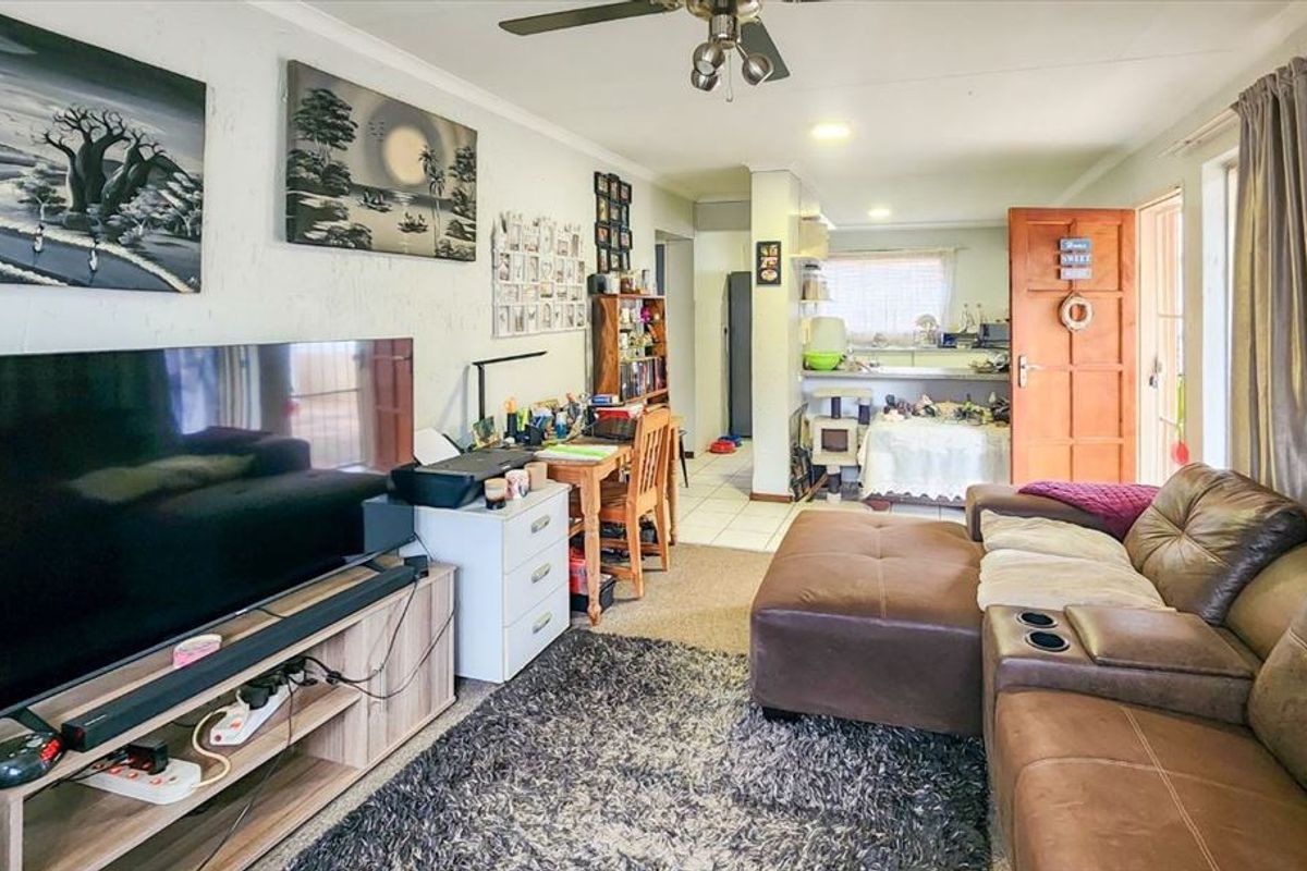 Open plan living area featuring a ceiling fan and tiled flooring, flowing into a functional kitchen space with a breakfast counter.
