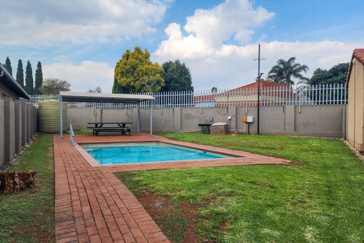 Private rear garden featuring a swimming pool, paved walkway, covered patio area, and perimeter walling.