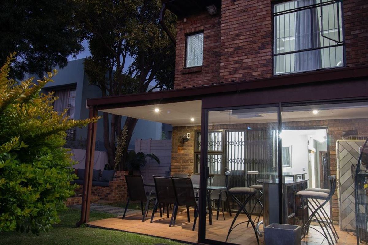 A covered patio area featuring brick exterior walls, recessed lighting, and sliding glass doors, providing a seamless transition to the garden space.