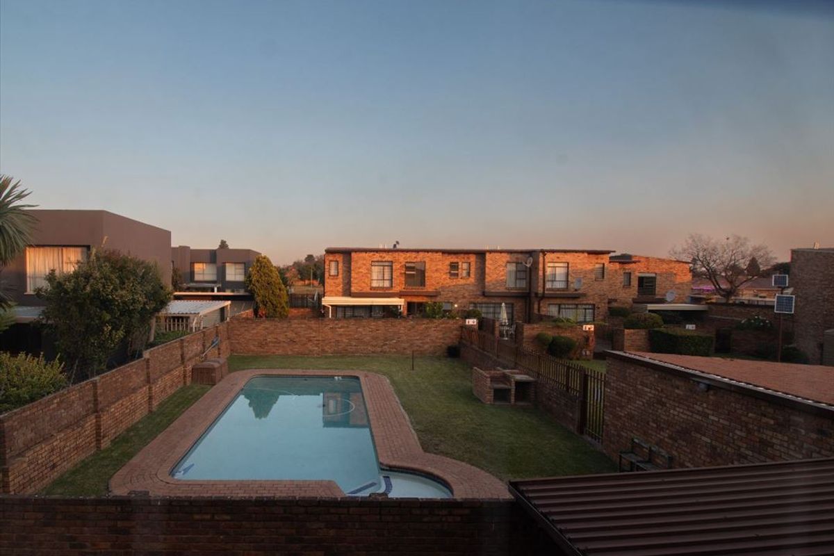 An elevated view of a communal townhouse complex featuring a swimming pool, brick boundary walls, and established garden areas.