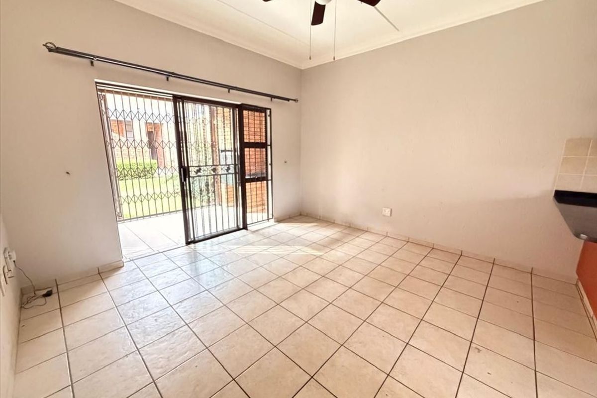 Open plan living area featuring tiled flooring, a ceiling fan, and sliding glass doors with security gates leading to an outdoor patio.