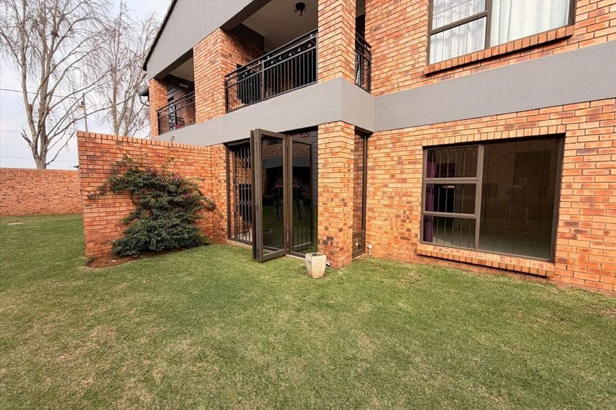 Rear view of a double-story townhouse featuring face-brick exterior, a private garden, and a balcony with metal railings.