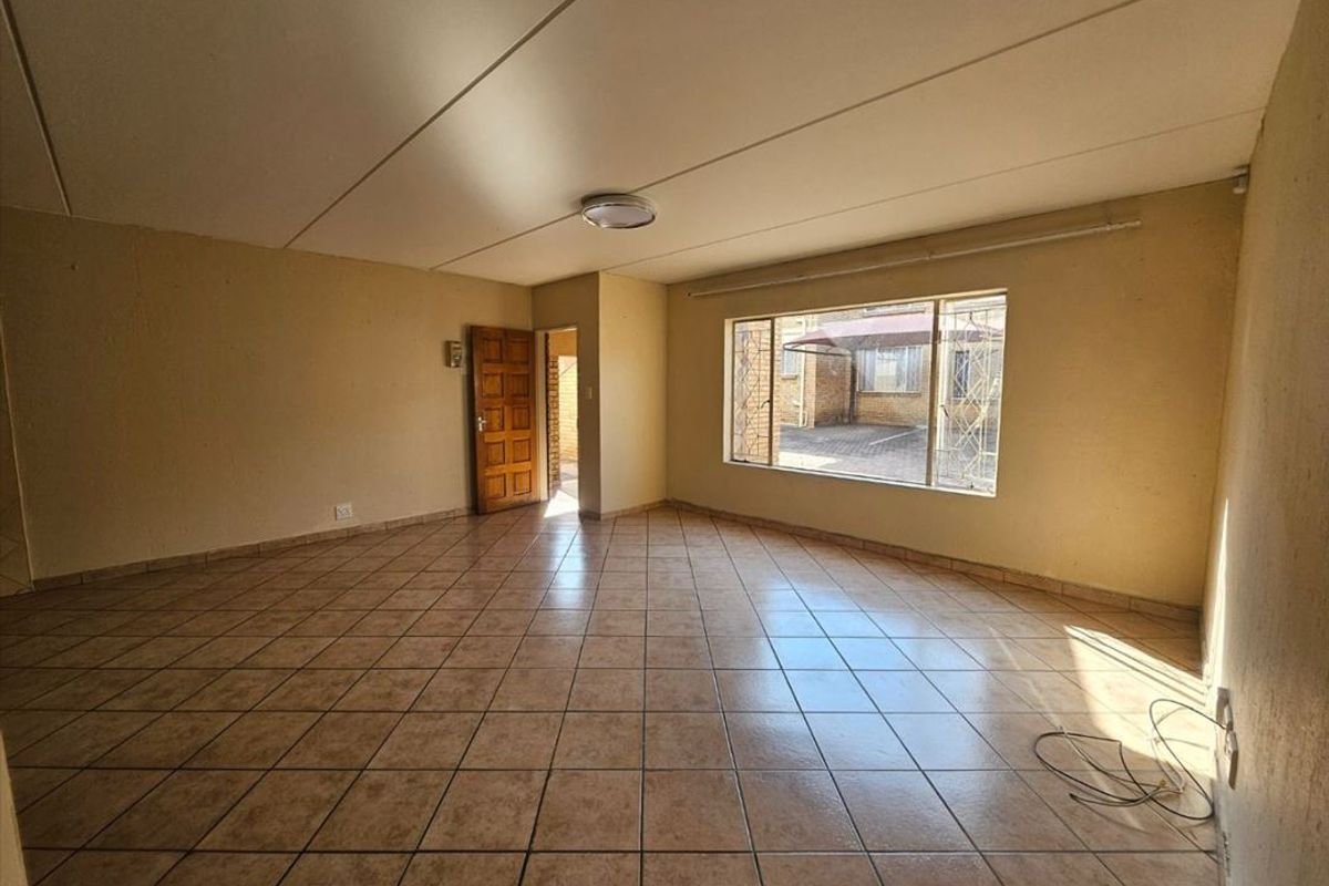 A spacious, empty living area featuring neutral tiled flooring, large windows providing natural light, and a solid timber entrance door.