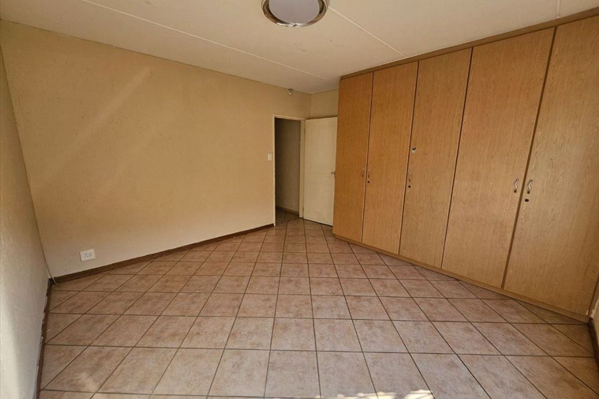 A spacious bedroom featuring built-in wooden cupboards and tiled flooring, offering a functional and neutral living space.