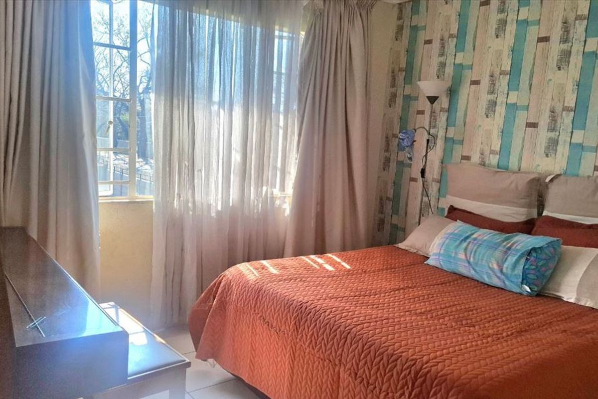 A bedroom featuring a large window with natural light, tiled flooring, and a decorative accent wall.