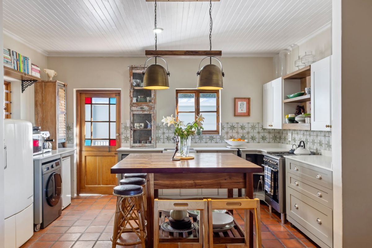 A charming kitchen featuring terracotta floor tiles, a central wooden island, patterned backsplash tiling, and a mix of open shelving and cabinetry.