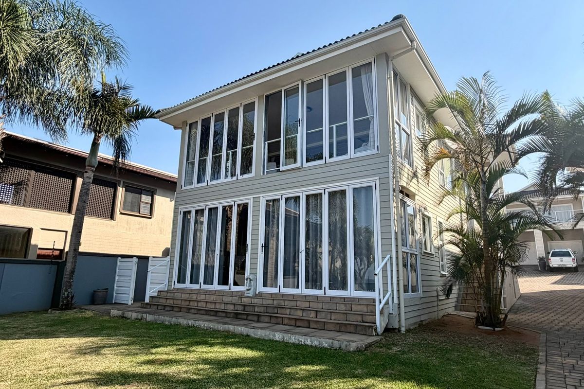 Rear view of a two-story townhouse featuring extensive glass folding doors on both levels, leading to a paved patio and private garden area.