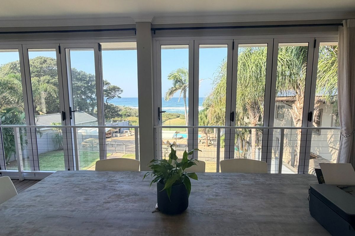 Bright living area featuring expansive floor-to-ceiling folding glass doors that open to a balcony with scenic coastal and garden views.