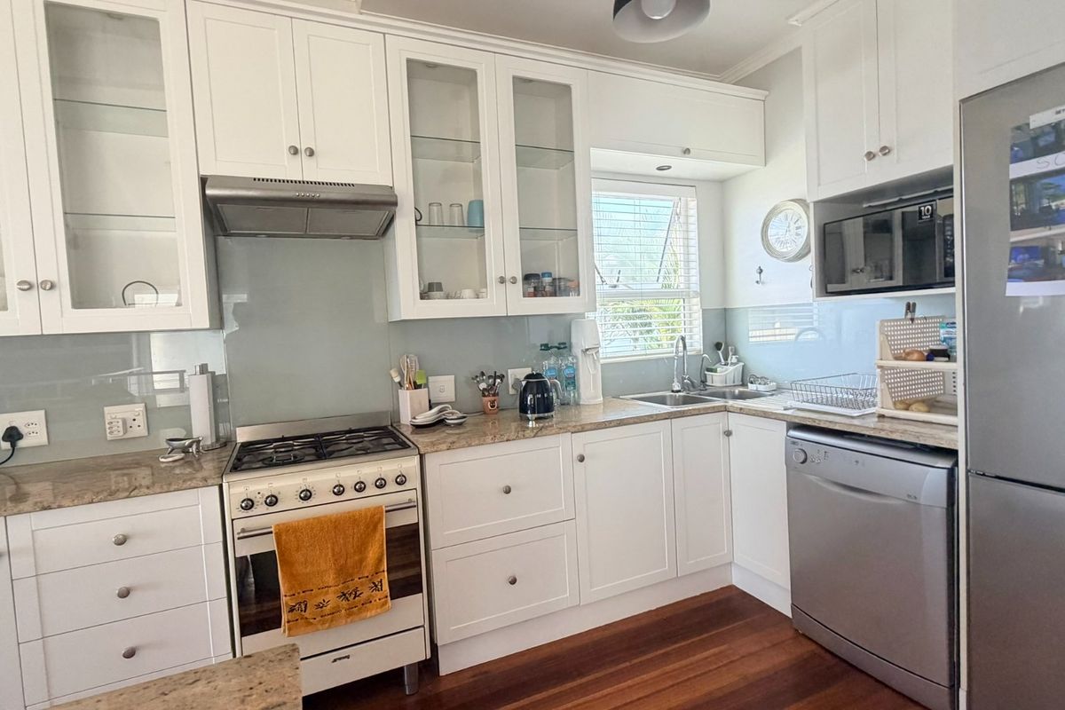 A well-maintained kitchen featuring white cabinetry, stone countertops, a gas stove with extractor fan, and integrated dishwasher space.