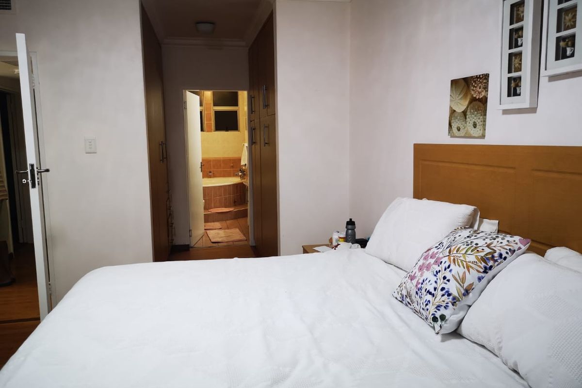 A bedroom featuring built-in wooden cupboards and an en-suite bathroom with a bathtub visible through the doorway.