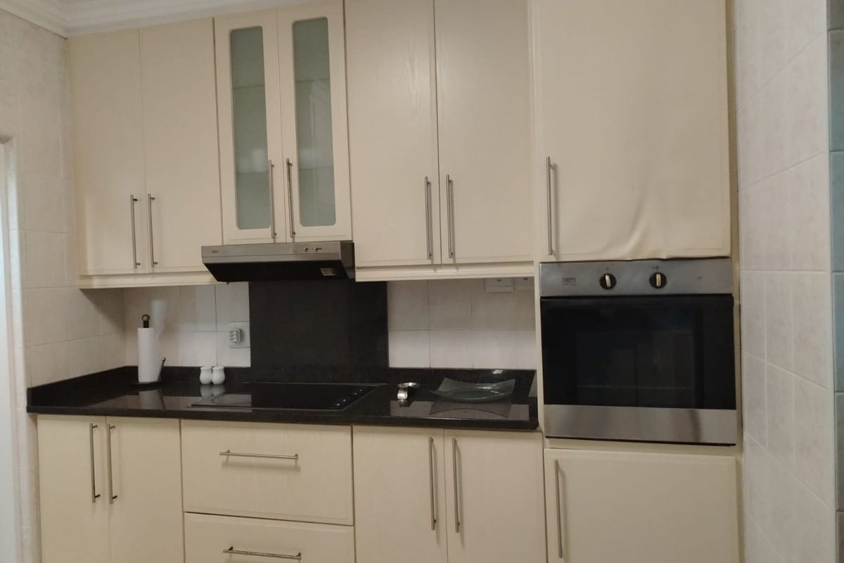 A functional kitchen featuring cream-colored cabinetry, dark granite countertops, a built-in oven, and an integrated extractor fan.