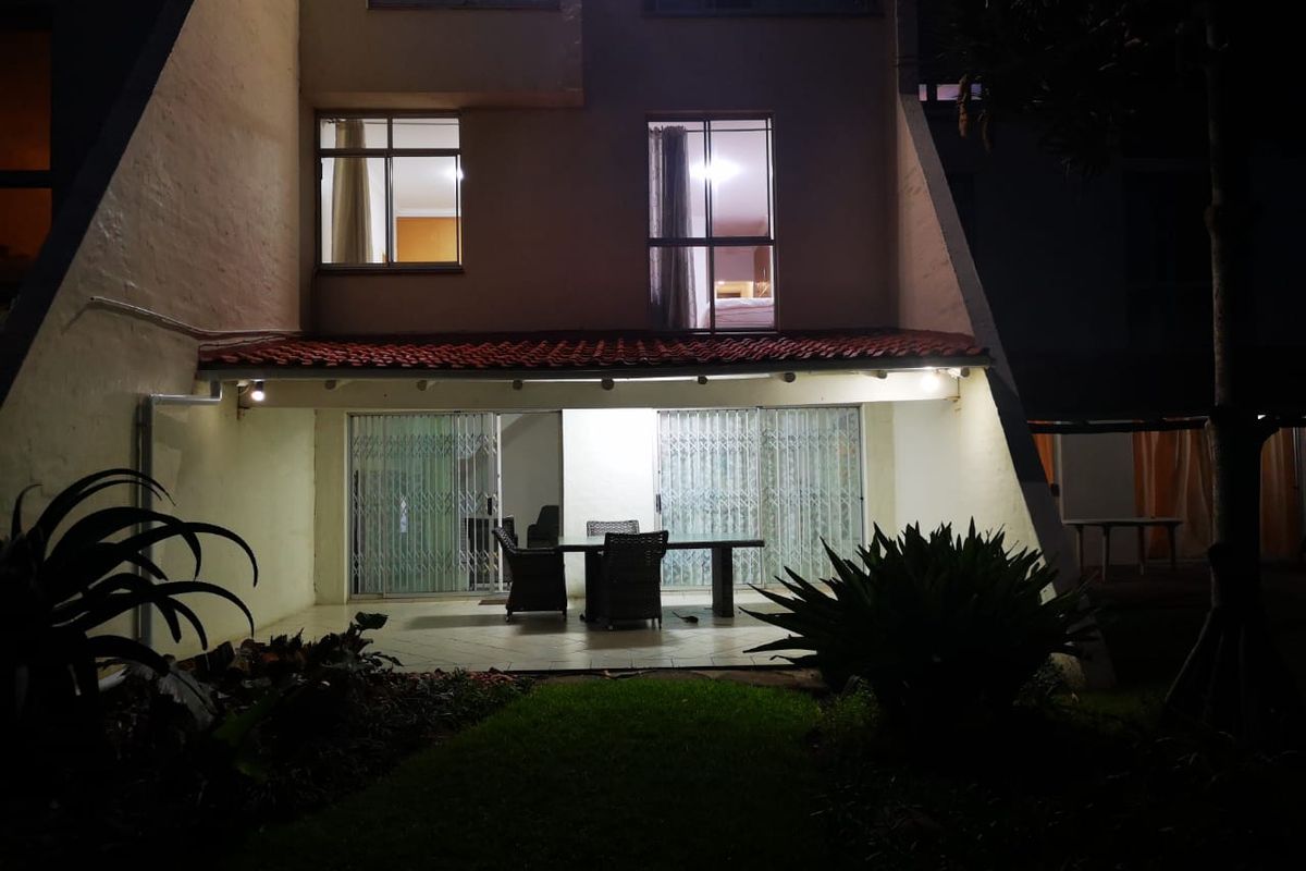 Night view of the apartment rear facade featuring a covered patio area with tiled flooring and security gates leading into the living space.