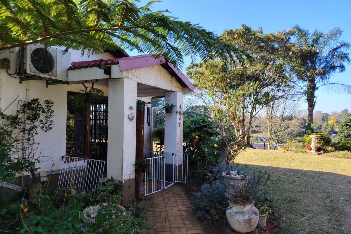 A charming exterior view of the property featuring a covered entrance porch, brick pathway, and a spacious garden area with mature trees.