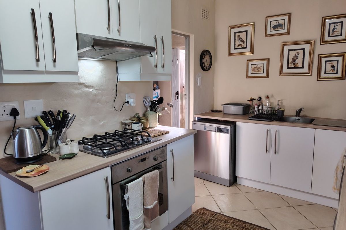 A functional kitchen featuring white cabinetry, a gas hob, built-in oven, stainless steel extractor fan, and integrated dishwasher space with tiled flooring.