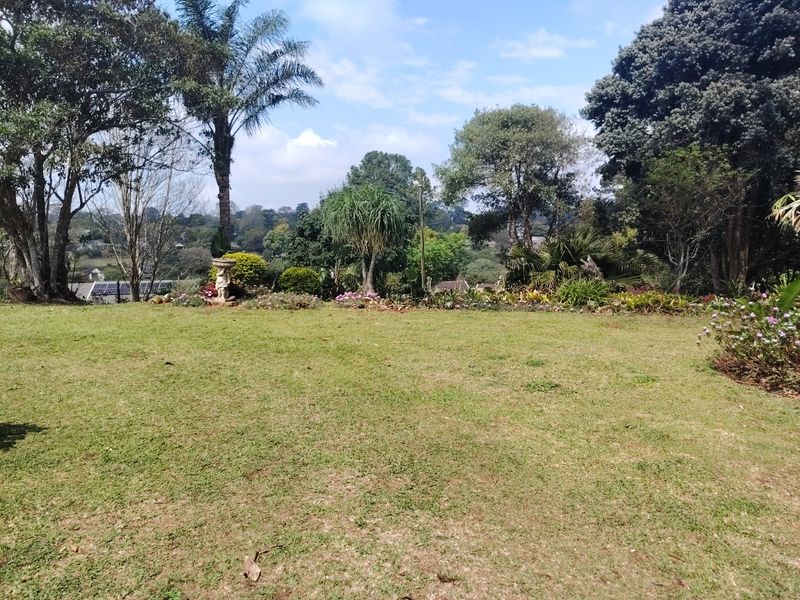 A spacious, well-maintained garden featuring a large lawn area surrounded by mature trees and established landscaping.