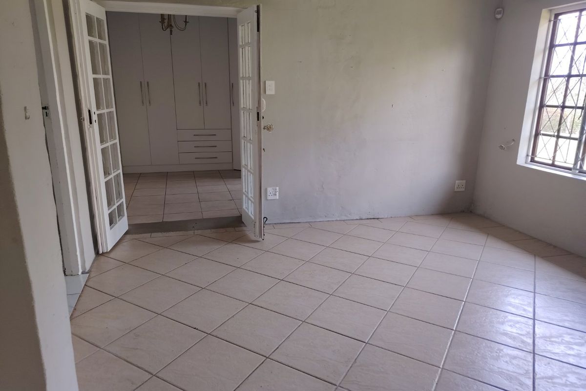 An empty living area featuring tiled floors and french doors leading to an adjacent room with built-in storage cupboards.