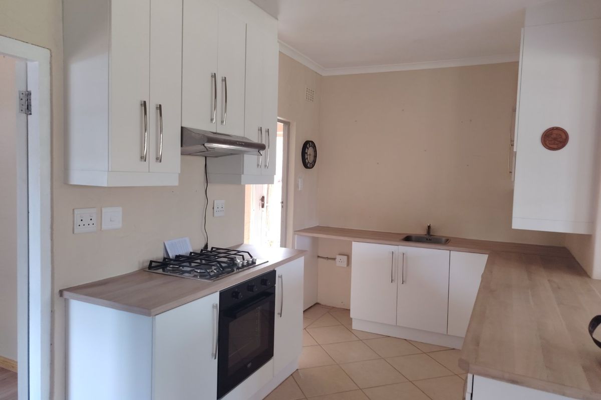 A clean, functional kitchen featuring white cabinetry, light wood-look countertops, a gas hob, built-in oven, and tiled flooring.