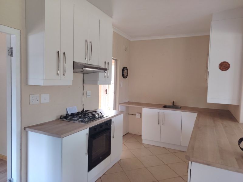 A clean, functional kitchen featuring white cabinetry, light wood-look countertops, a gas hob, built-in oven, and tiled flooring.