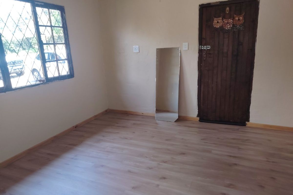 A vacant bedroom featuring light-toned laminate flooring, timber skirting boards, and a wooden door, with security bars installed on the window.