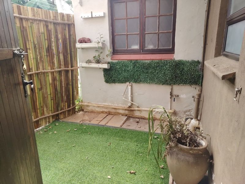 A small rear courtyard area featuring artificial turf, a bamboo privacy screen, and external wall finishes requiring maintenance.