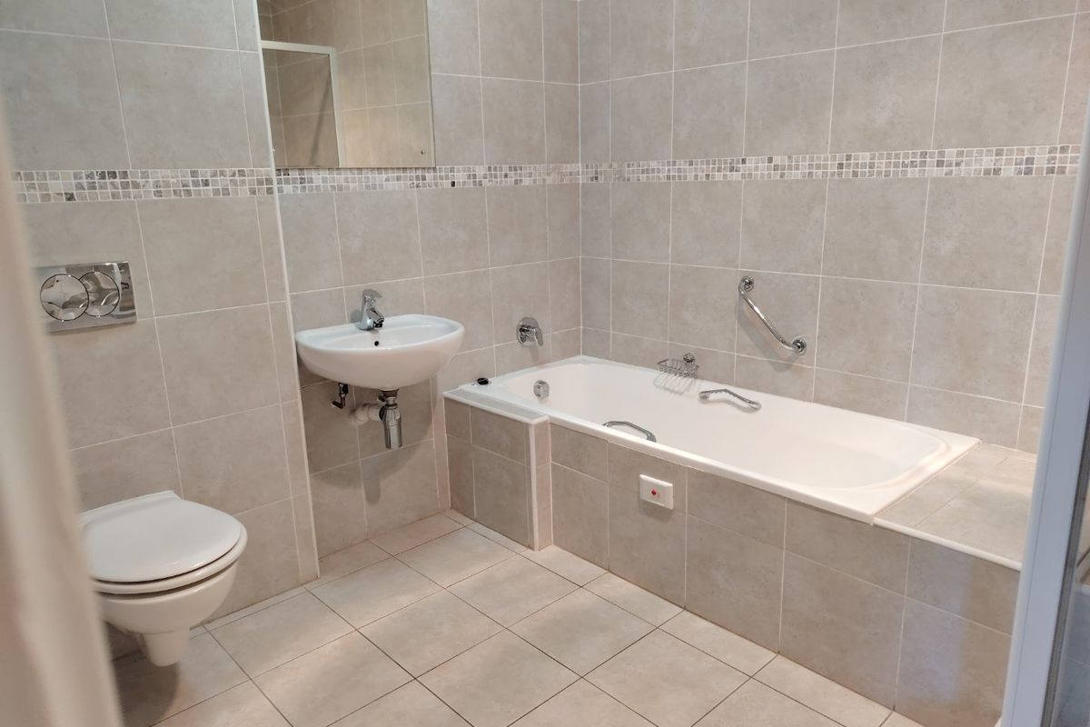 A clean, neutral-toned bathroom featuring a built-in bathtub, wall-mounted basin, and a wall-hung toilet with integrated flush plate.