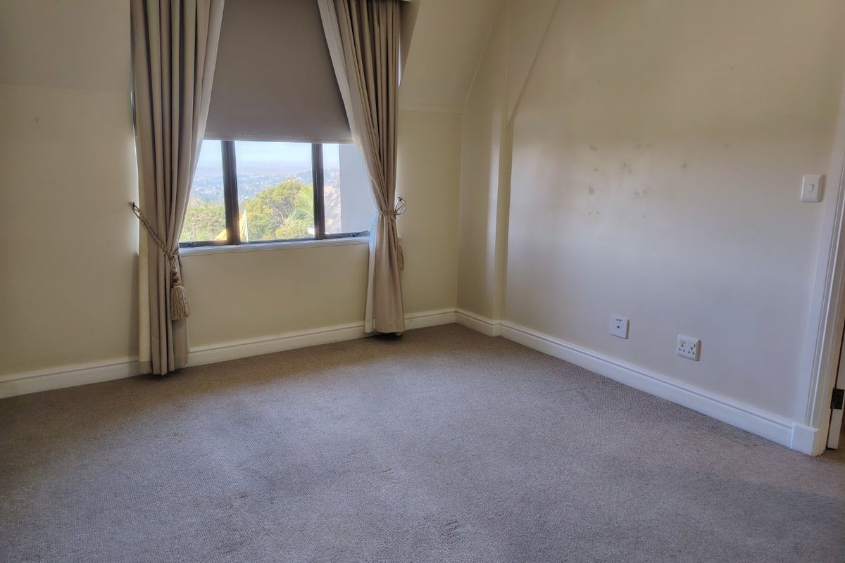 A vacant bedroom featuring neutral carpeting, built-in curtain tracks, and a window with views of the surrounding area.