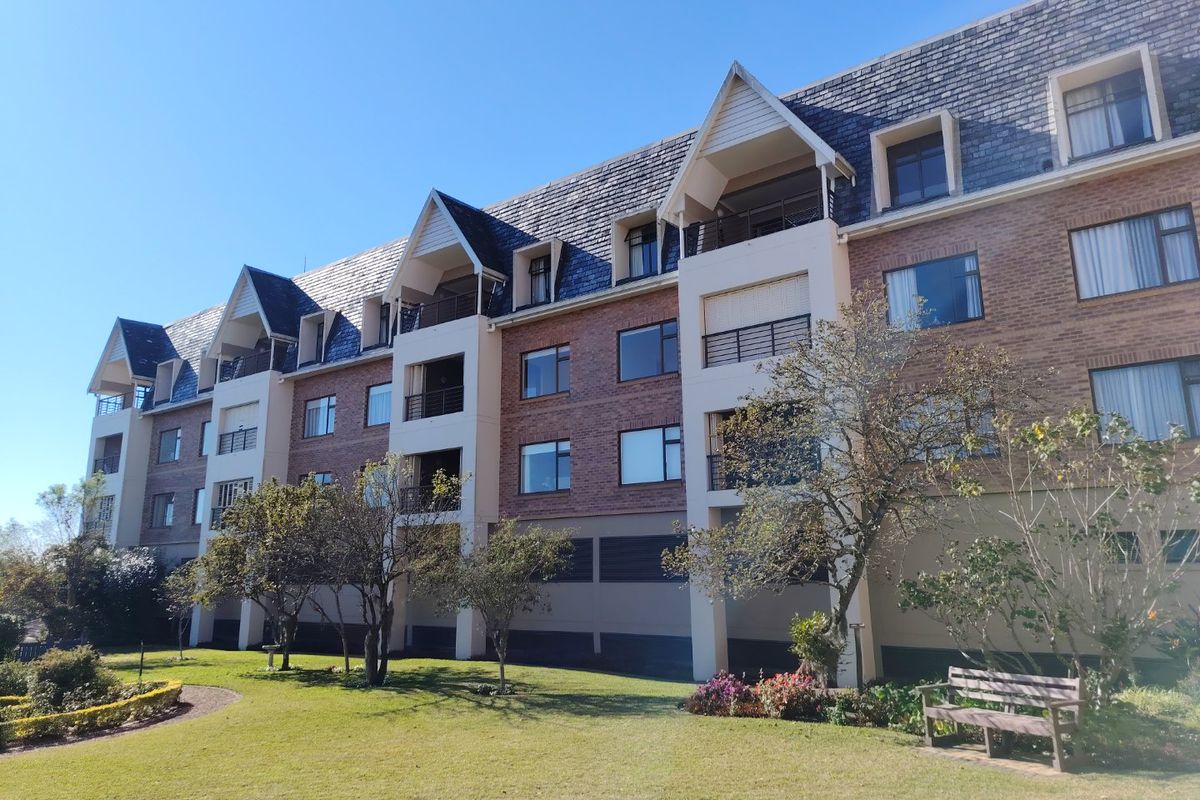 A view of the apartment building exterior featuring brick facade, pitched slate roof, and multiple balconies set within a landscaped garden area.