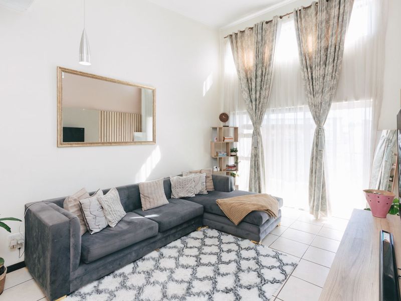 Bright and airy living room featuring high ceilings, large windows with floor-to-ceiling curtains, and neutral tiled flooring.