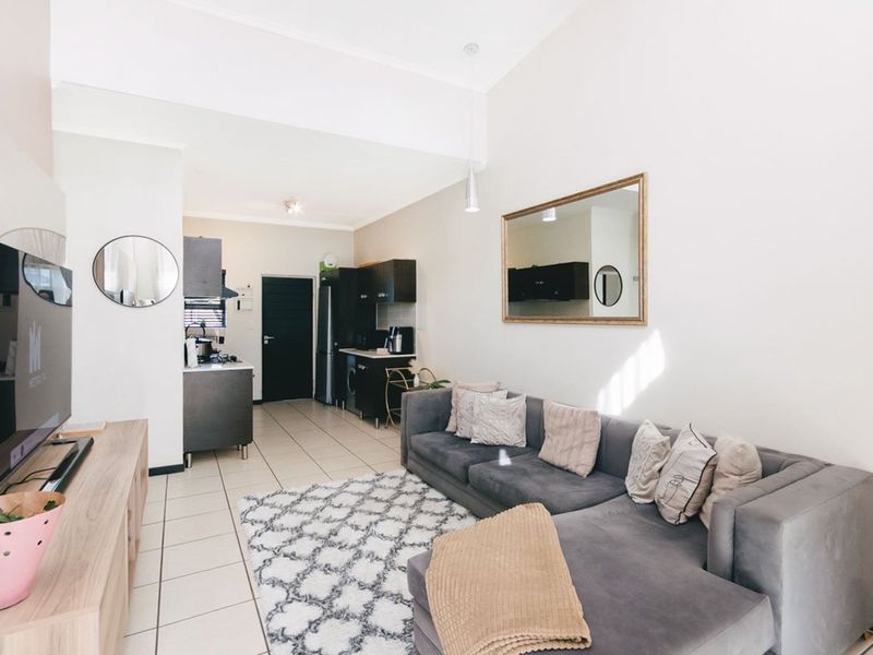 An open-plan living area featuring tiled flooring and a compact kitchen with dark cabinetry, seamlessly flowing into the lounge space.