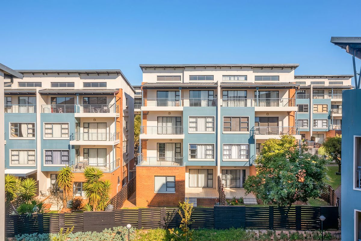 Exterior view of a modern multi-story apartment complex featuring balconies, brick and painted facade finishes, and landscaped grounds.
