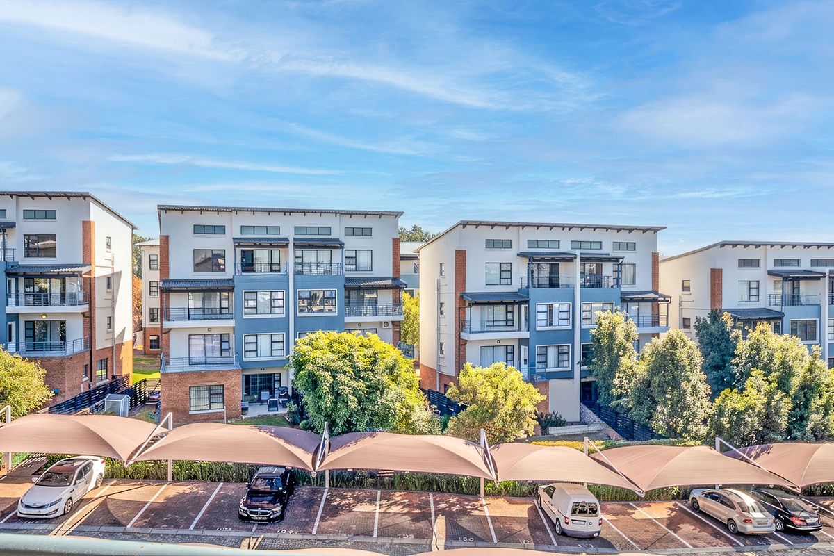 An elevated view of a modern apartment complex featuring multi-story residential buildings, landscaped grounds, and covered parking bays.